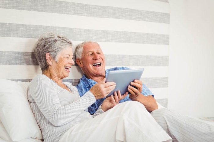 Senior couple laughing while using digital tablet in bedroom