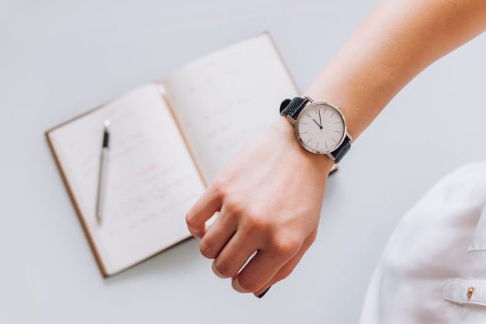 A young business woman checks time on her classic watch, she thinks about time management and corrects schedule in her diary