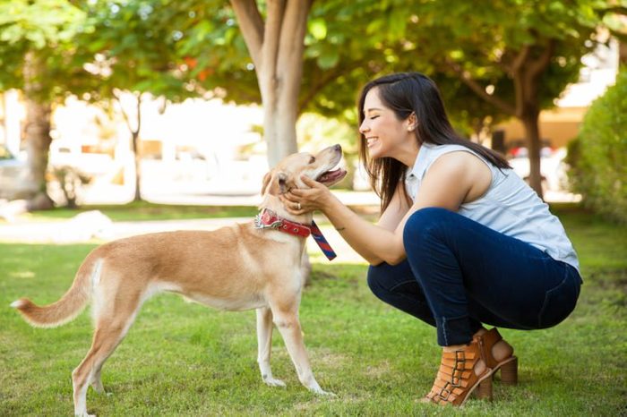 Profile view of a beautiful young woman petting her dog and giving it a kiss at a park