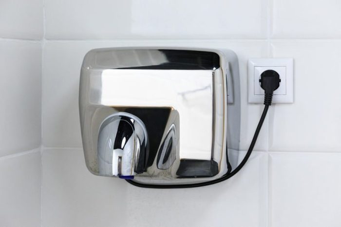 Metal hand dryer on the white tiled wall