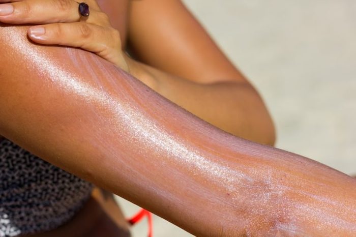 Close up on woman's upper arm and hand spreading sun cream at the beach on a hot, sunny day. Tanning, sunblock spread, skin care, ultraviolet rays protection, cancer prevention concept