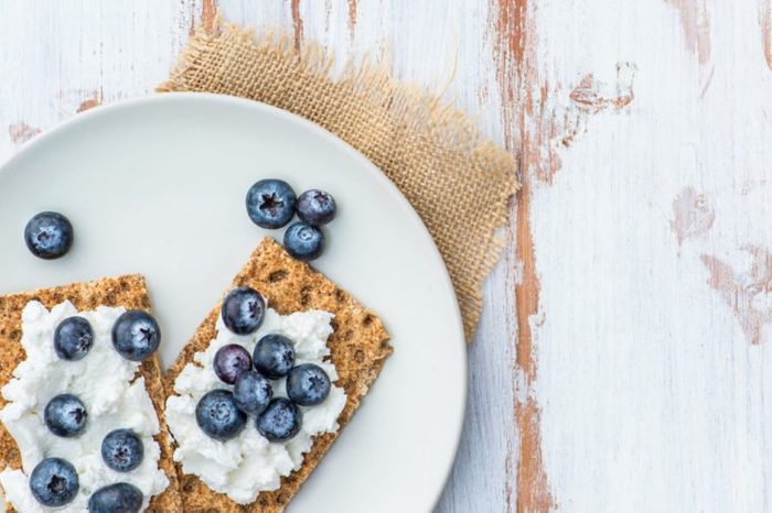 Healthy Snack from Wholegrain Rye Crispbread Crackers with Ricotta Cheese and Fresh Blueberries on the Light Background