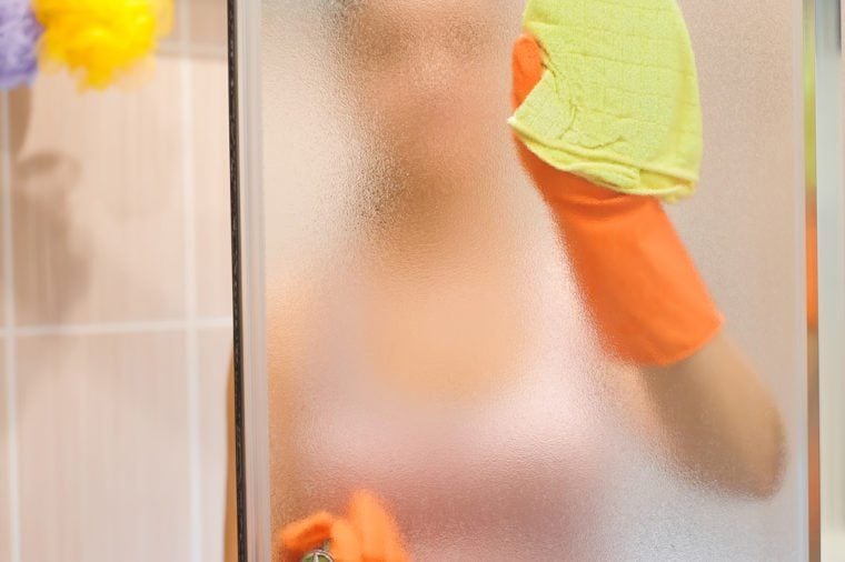 young woman cleaning shower door