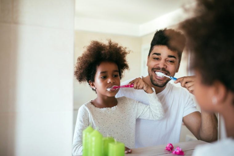 Portrait of happy african american father and daughter brushing teeth in the bathroom.