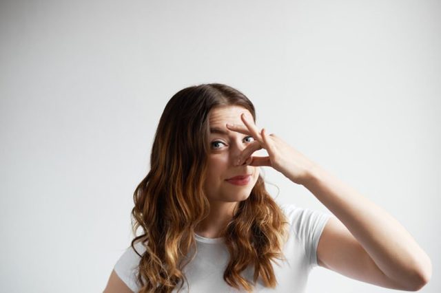 Bad smelling concept. Studio shot of disgusted young European woman pinching her nose because of awful stink coming out from garbage or spoiled food. Negative human emotions and nasty feelings.