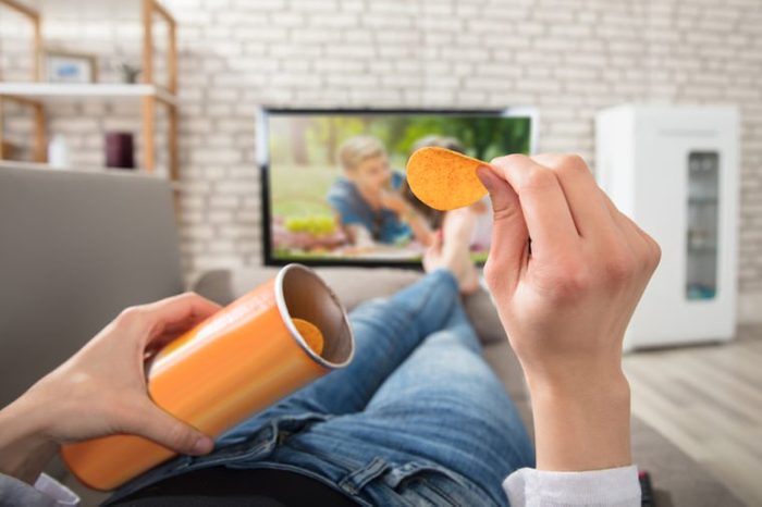 Close-up Of A Woman Eating Potato Chips While Watching Television