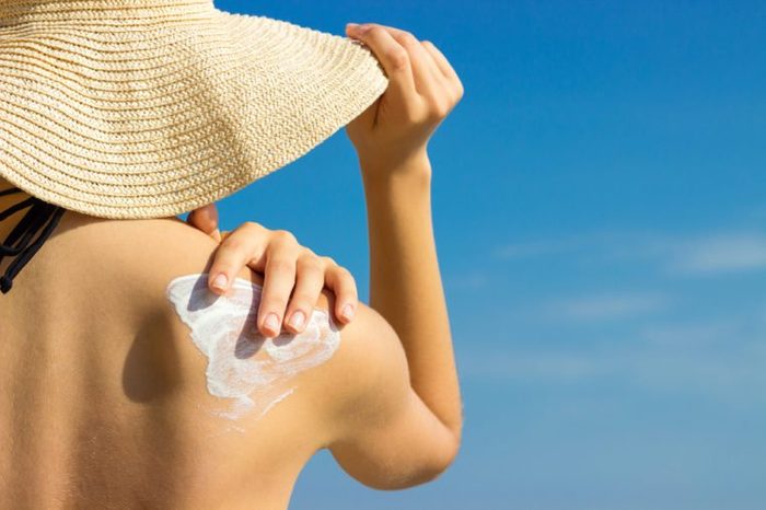 Sunscreen sunblock. Woman in a hat putting solar cream on shoulder outdoors under sunshine on beautiful summer day.