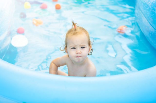 Sixteen months old baby girl playing in the plastic pool with her toys; baby covered with sun protection cream; happy and care free childhood concept