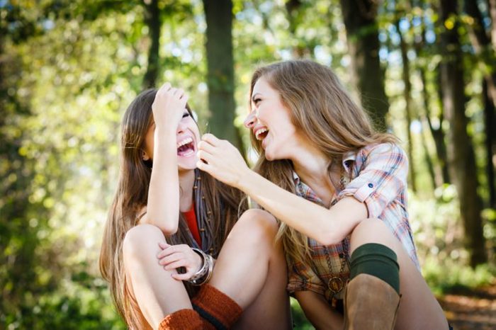 two young beautiful females laughing talking having good time sitting in park