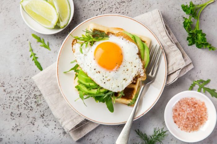 savory waffles with avocado, arugula and fried egg for breakfast, top view
