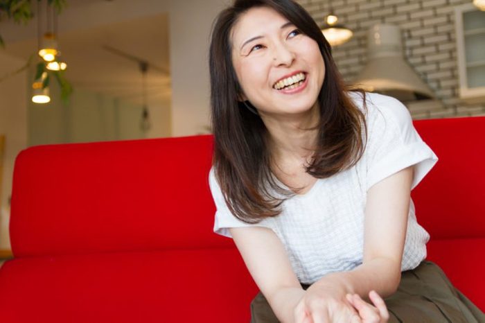 Japanese woman laughing at living room, sitting on red sofa