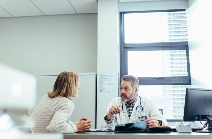 Male physician talking to a patient during consultation at his office. Mature doctor explaining diagnosis to female patient.