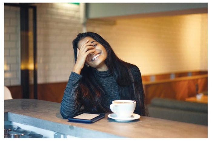 Portrait of a young, attractive and elegant Indian Asian lady in a warm and cosy cafe. She is laughing in a natural, relaxed manner.