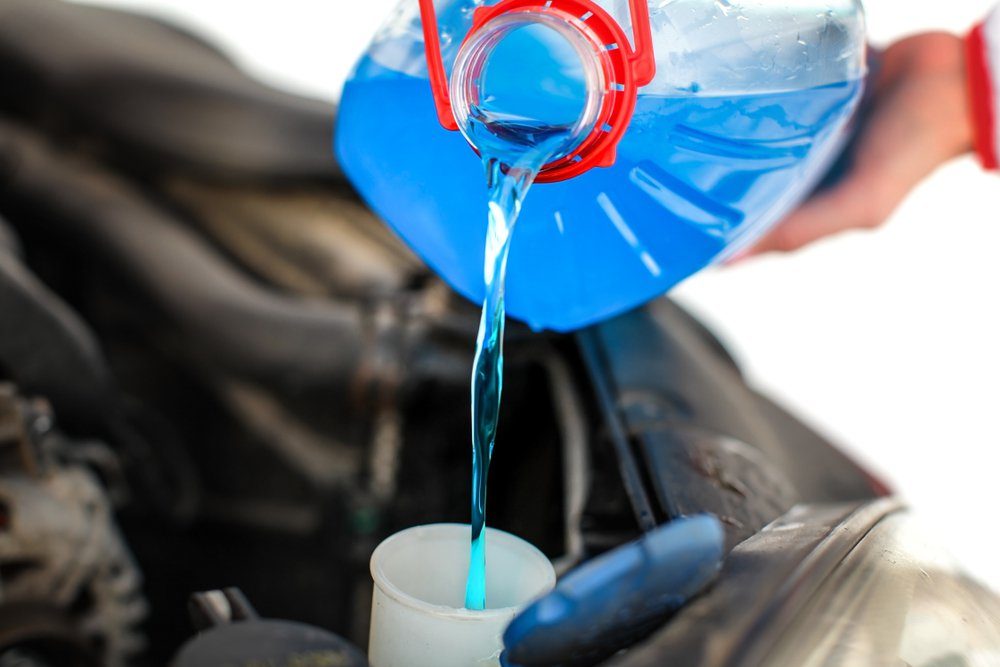 Woman pouring blue antifreeze liquid into dirty car.
