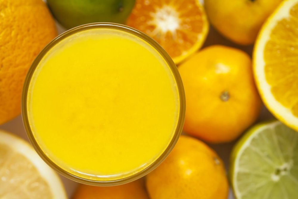 An overhead image of a glass with citrus juice, surrounded by citrus fruit.