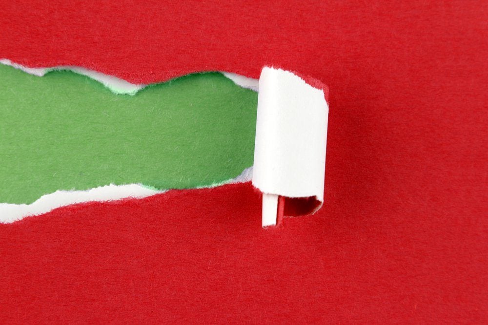 Hole ripped in red paper on green background. Copy space