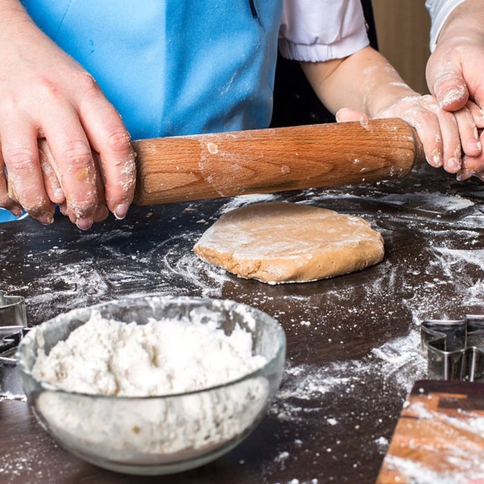 Hands of little girl sheeting dough with rolling pin.
