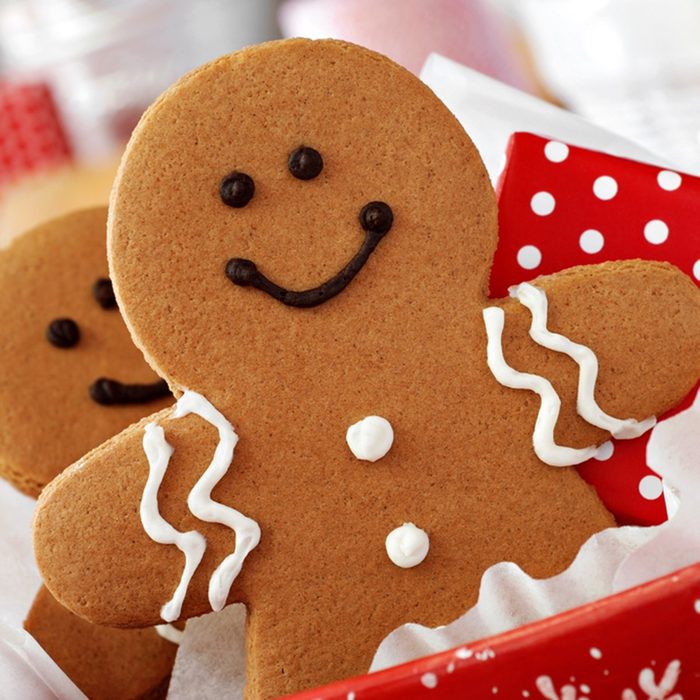 Smiling gingerbread men nestled in holiday dish with gift-wrapped surprise.