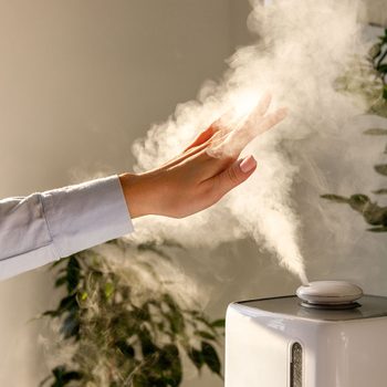 Humidifier hack - Woman holds hand over steam aroma oil diffuser on the table at home