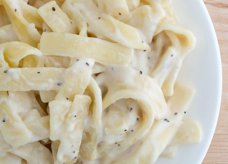Top close view of a fettuccine alfredo TV dinner on a plate on a wood table top illuminated with natural light.