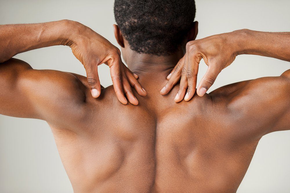 Muscular black man. Rear view of young muscular black man touching his shoulders while standing isolated on grey background