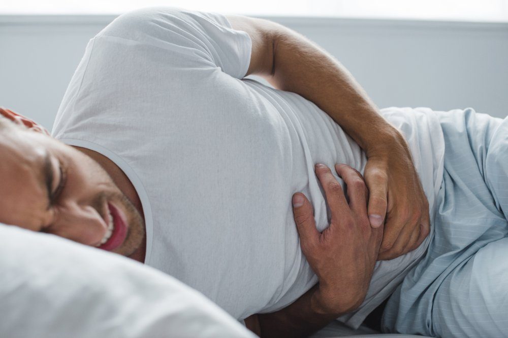 cropped shot of man suffering from stomach pain in bed