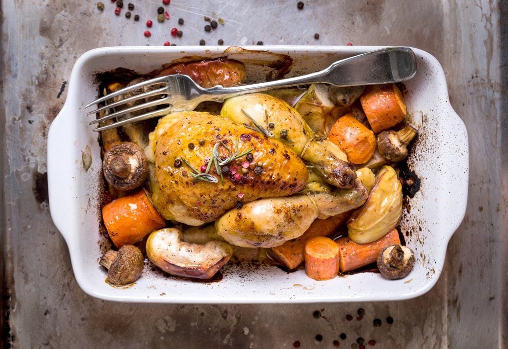 Whole baked juicy chicken with golden crispy skin. Roasted chicken in baking dish with apples, carrot, mushrooms, rosemary, garlic, pepper on rustic iron oven-tray. Overhead. Dinner. Cooked poultry 