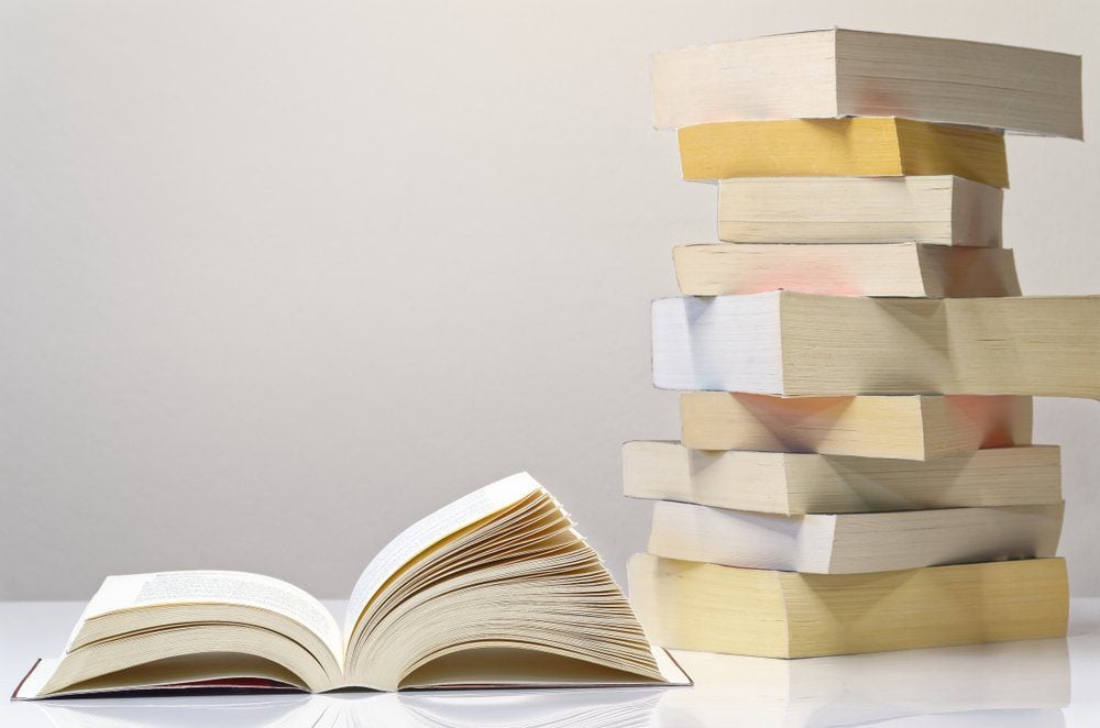 Open book and pile of books on the white table with light grey background