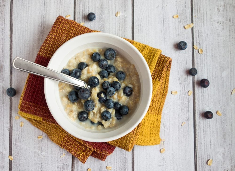 A healthy bowl of hot oatmeal with blueberries with spoon sitting on a light wood surface.
