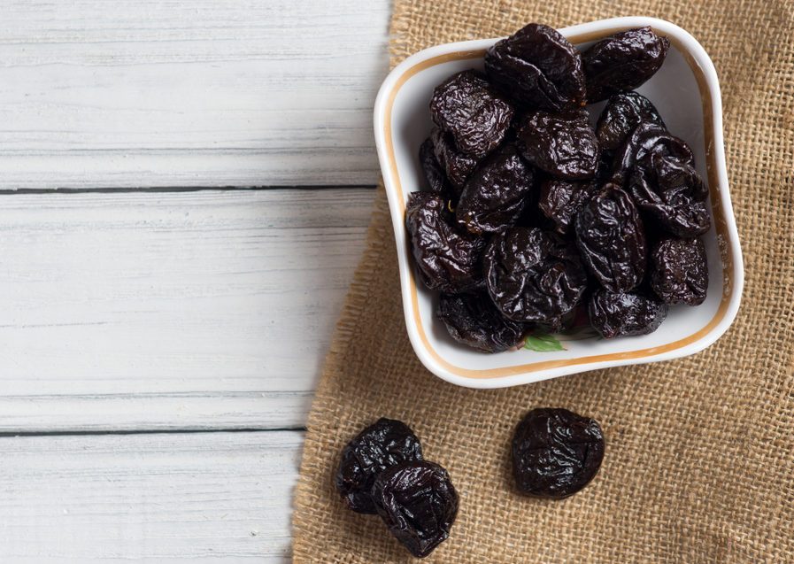 Prunes in bowl on wooden white background