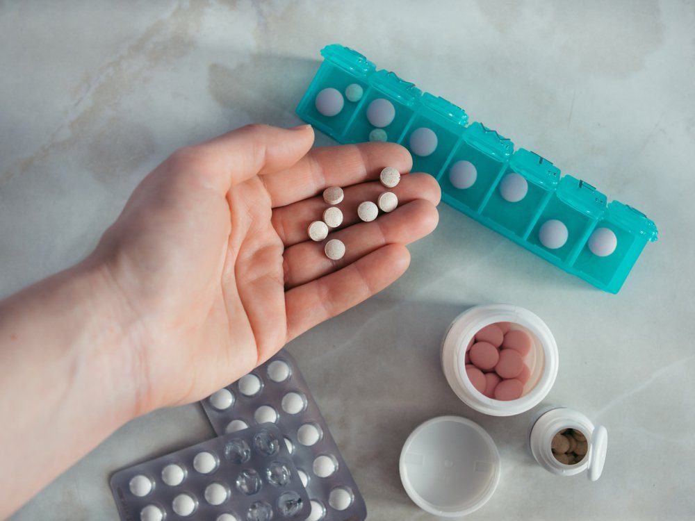 Hand with pills and pillbox. Top view of seven day pill box with pills. Green pill-box over light marble table. Open pill box and open boxes with pills or vitamins. Copy space. Top view or flat-lay.