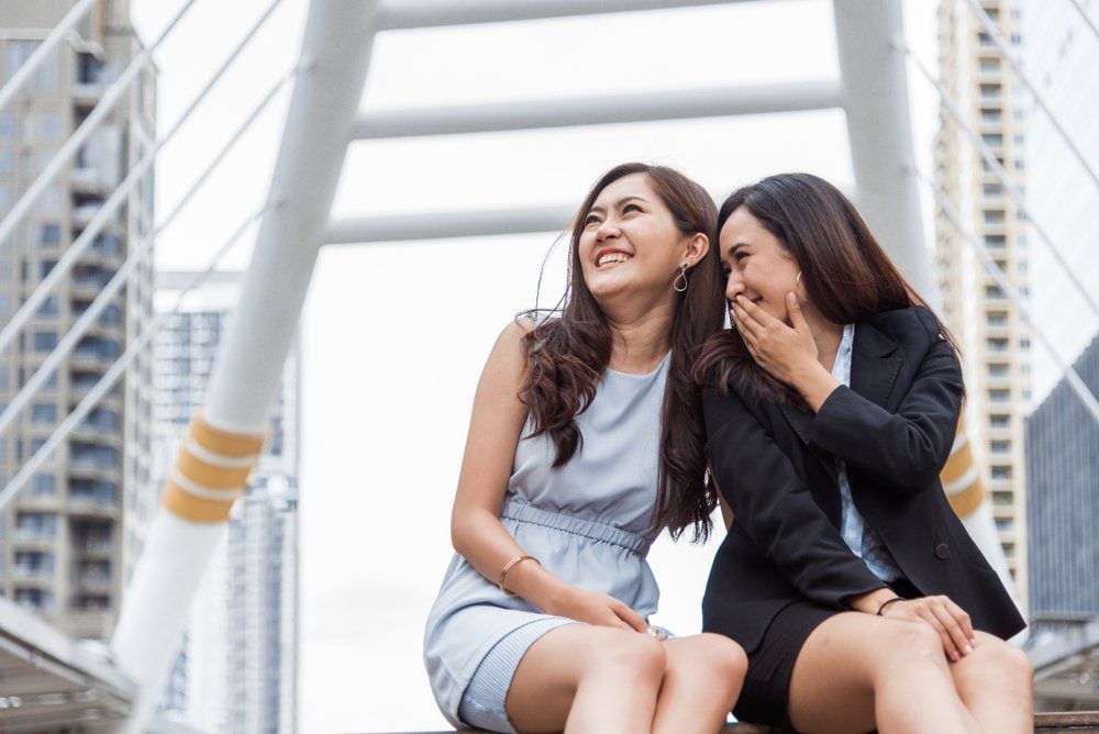 Two Asian businesswomen gossip joke story at outdoors city after finished working. Business women coworker and friendship concept. Beautiful business people talking secret scandal topic in office life