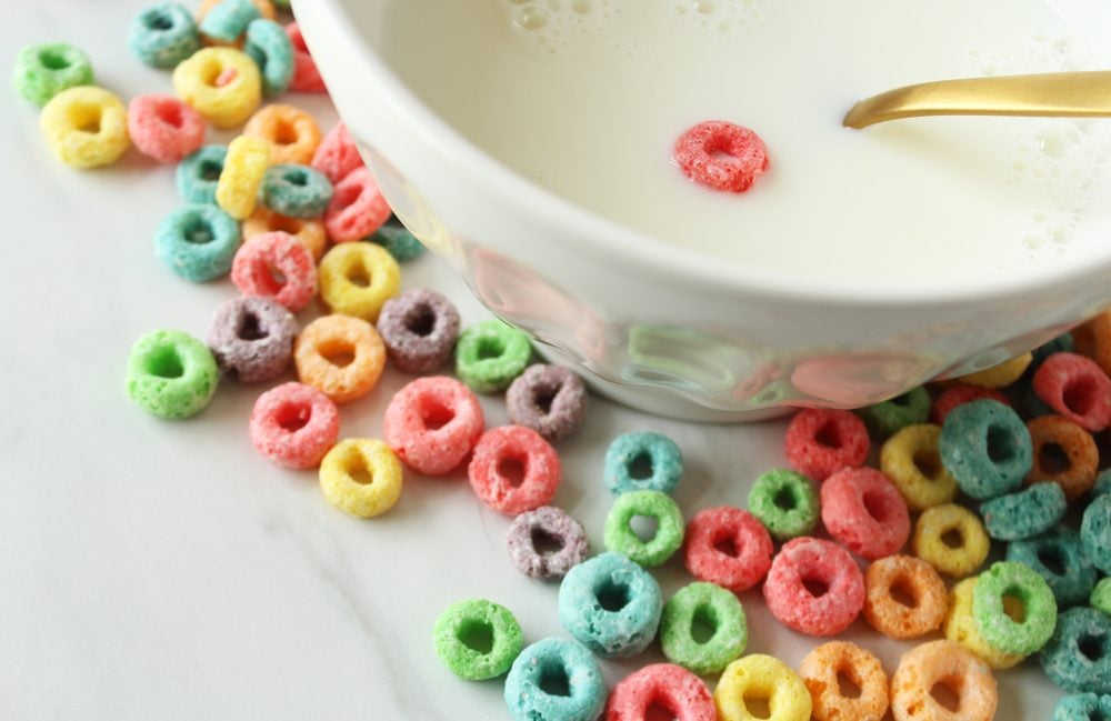 Close up view of cereal bowl with one piece of cereal and dry cereal spilled around it. Empty calories concept. Copy space.