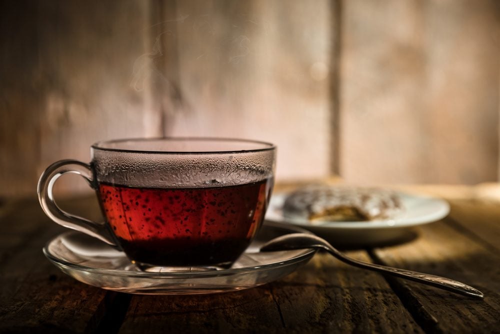 Glass cup of black tea, teaspoon and honey cake on wooden table