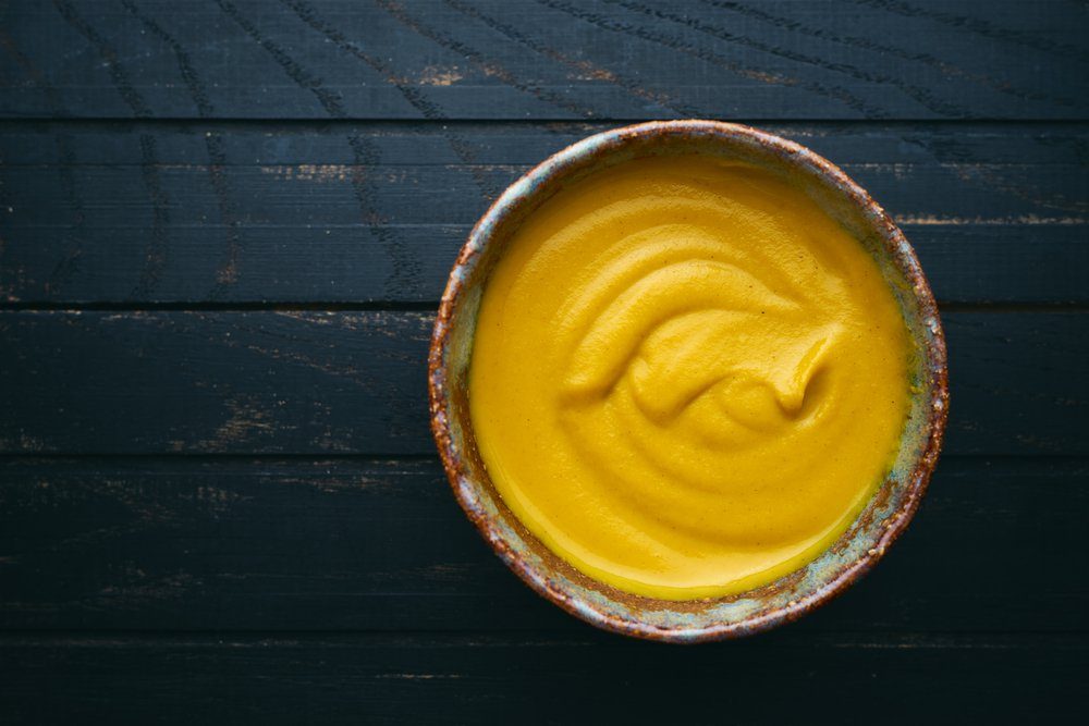 Fresh homemade organic mustard in bowl on wooden background top view