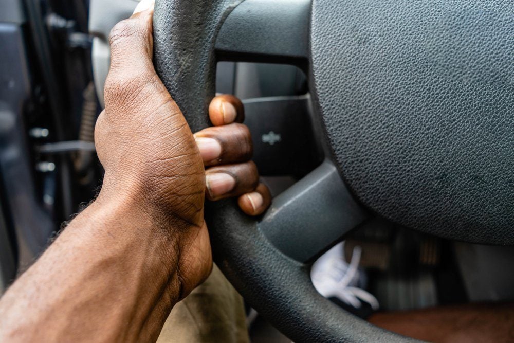 Close-up Of A Black African American Man Hands Holding Steering Wheel While Driving Car. Detail of a hand holding a steering wheel.