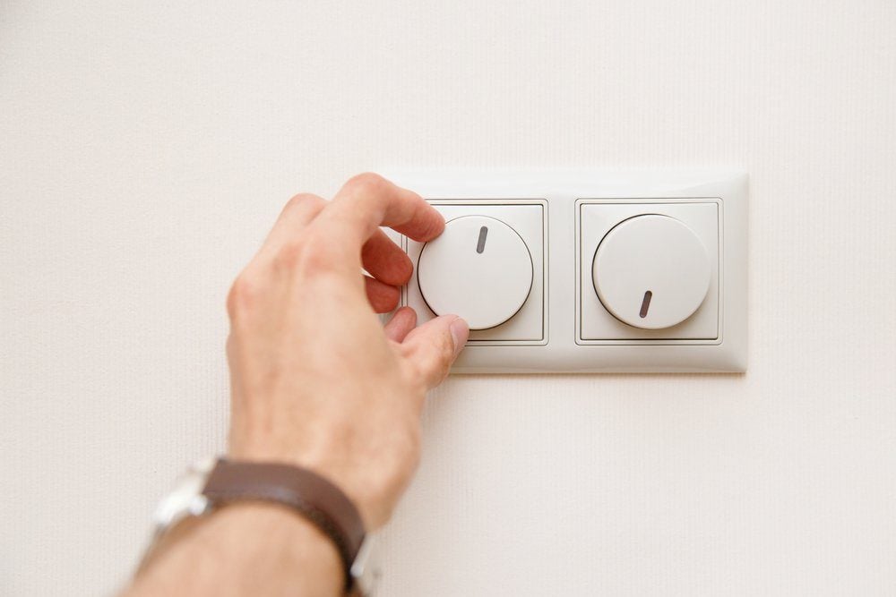 Saving energy concept: Human hand turning down electrical light dimmer switch.