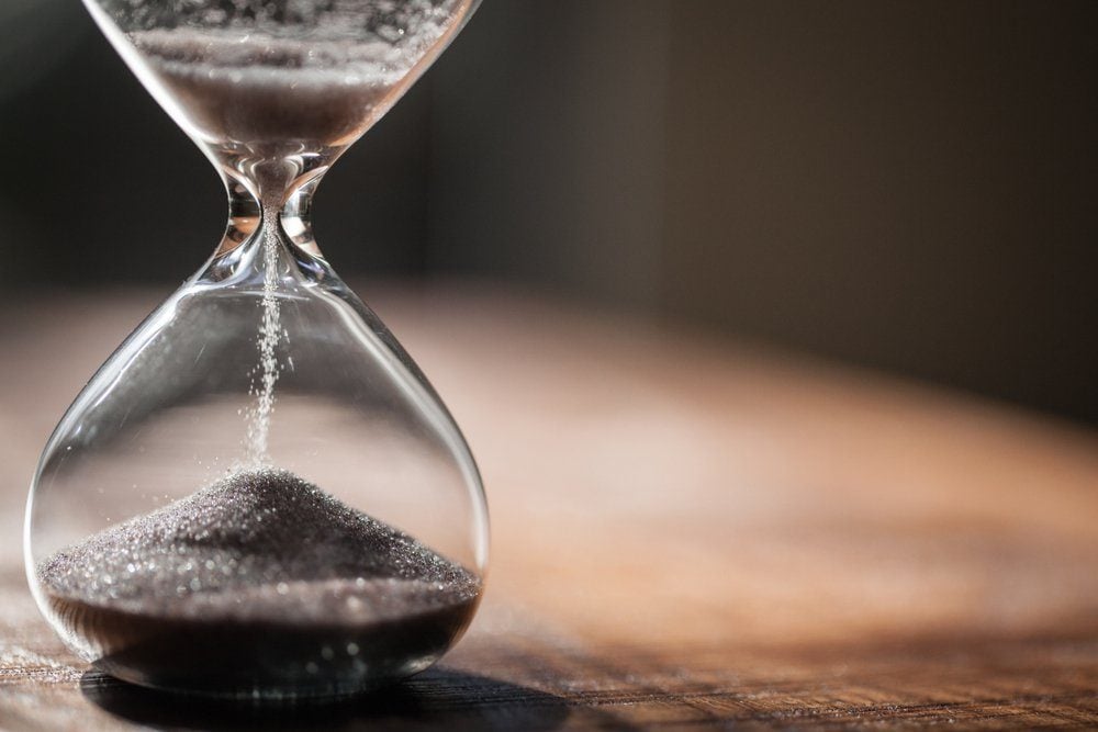Hourglass as time passing concept for business deadline, urgency and running out of time. Sandglass, egg timer on wooden floor showing the last second or last minute or time out. With copy space.