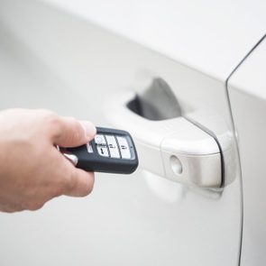 Human hand holding a keyless entry device or key fob to open the new car and start the car. focus on the keyless device system and door handle