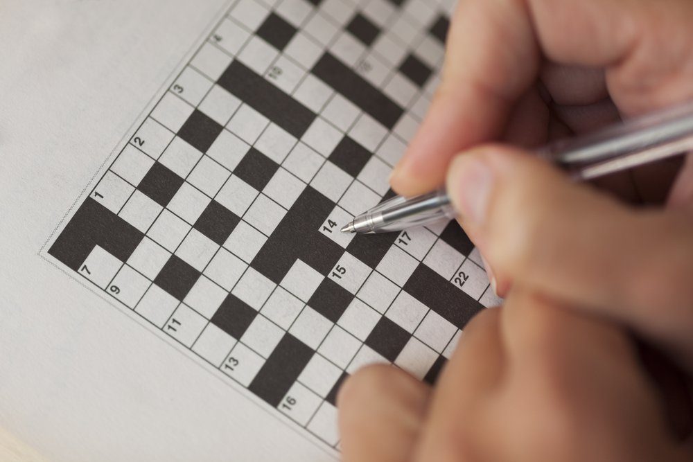 Woman's hand with ballpoint pen is filling crossword puzzle.