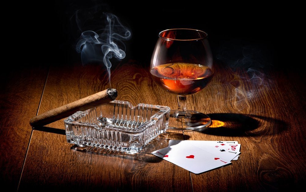 Playing cards near wineglass of whiskey and cigar