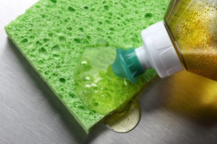 macro shot of dish soap being squeezed onto green sponge in aluminum sink