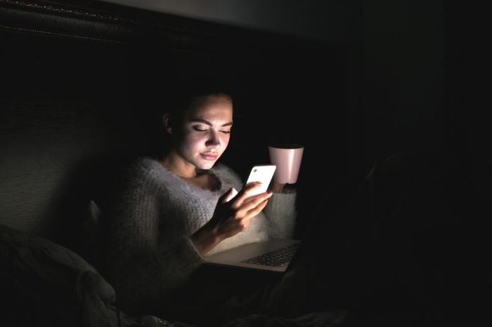 cute young girl sits in the dark at night, can not fall asleep and looks into her smartphone