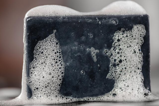 black charcoal carbon soap on black background with soap bublles foam