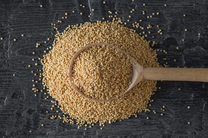 A pile of amaranth seeds and a wooden spoon on a dark wooden table. The view from the top.