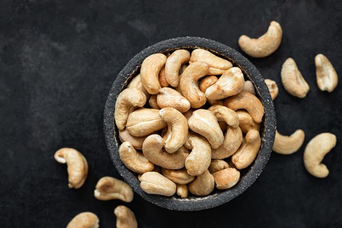Cashew nuts in bowl on black background. Top view, copy space for text. Healthy snack, vegetarian food, beer snack