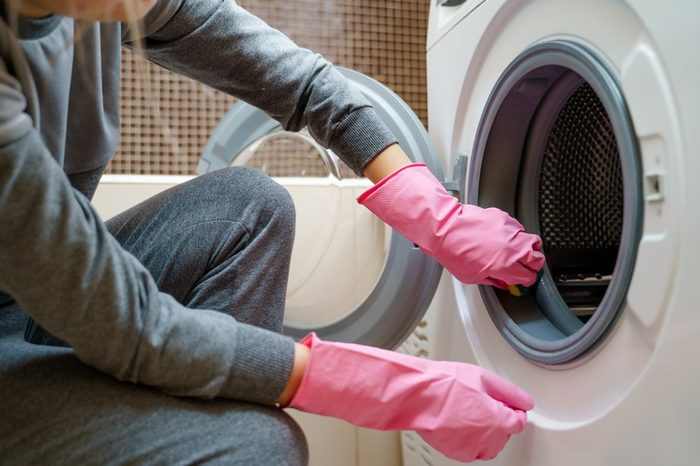 Image of female hands in pink rubber glove washing washing machine