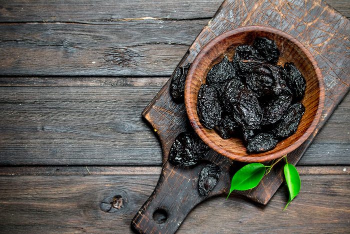 Foods everyone over 50 should be eating - Prunes with green leaves in the bowl. On a wooden background.