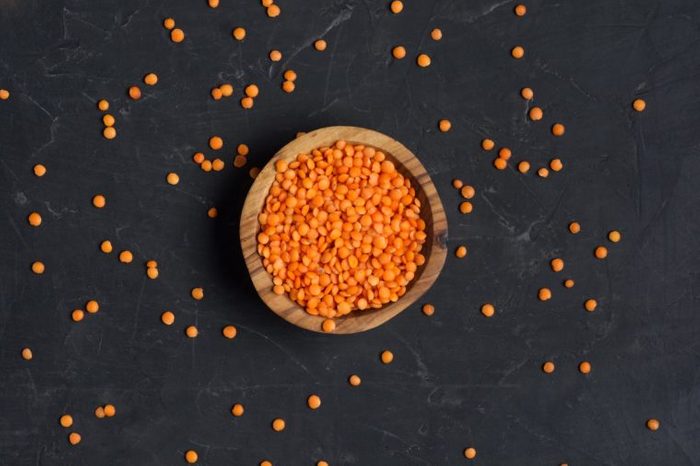 Red lentils in wooden bowl on a dark concrete background. Top view or flat lay