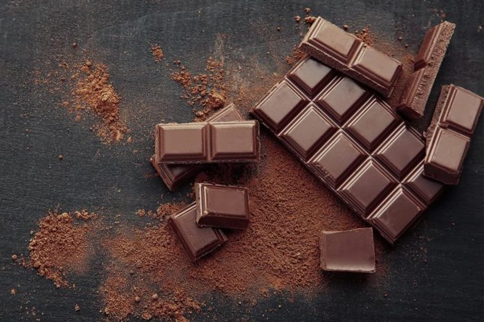 Разбитые кусочки шоколада и какао-порошок на деревянном фоне